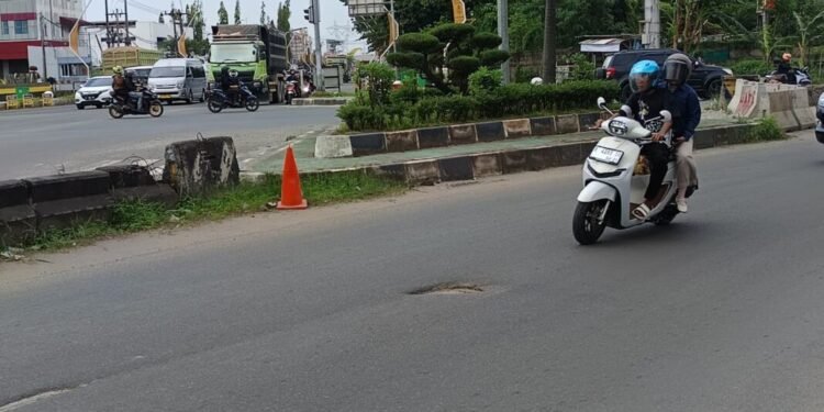 Pengendara motor menghindatri jalan berlubang yang ada di sekitar Kampus Merah Jalan Lingkar Selatan (JLS), Desa Serdang, Kecematan Kramatwatu, Minggu (1/3/2026). (Andika/Bantenraya.com)