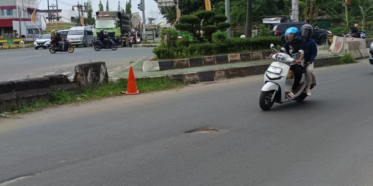 Pengendara motor menghindatri jalan berlubang yang ada di sekitar Kampus Merah Jalan Lingkar Selatan (JLS), Desa Serdang, Kecematan Kramatwatu, Minggu (1/3/2026). (Andika/Bantenraya.com)